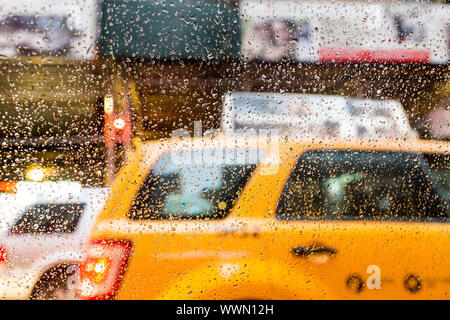 Close-up of raindrops on a glass window with a blurred yellow taxi and city lights in the background on a rainy day in New York City, USA Stock Photo