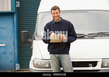 Deliveryperson standing with van writing in clipboard smiling Stock Photo