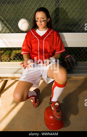 Softball Player Tossing Ball in Dugout Stock Photo