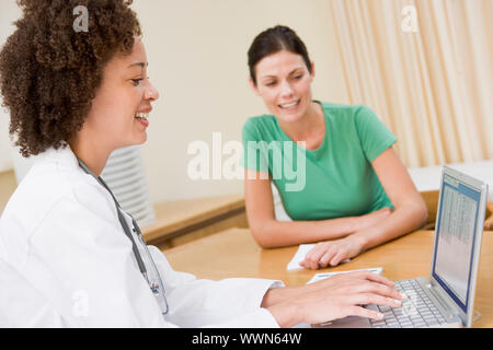 Doctor using laptop with woman in doctor's office smiling Stock Photo