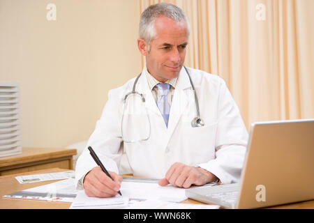 Doctor using laptop and writing in doctor's office Stock Photo