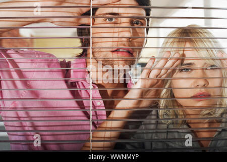 Couple Looking Through Venetian Blinds Stock Photo