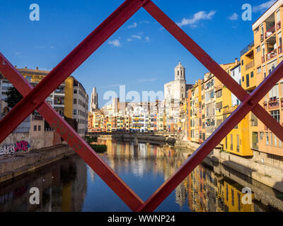 Girona's tipical skyline cityscape through the frame of red iron bridge over the Onyar River with colourful river houses on a blue sunny sky, Church o Stock Photo