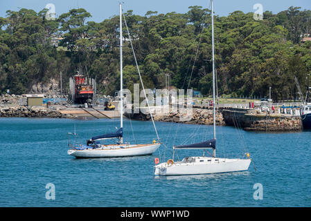 A large red fishing trawler vessel mounted on the slipway and two yachts moored in Ulladulla Harbour on a sunny Summers day Stock Photo