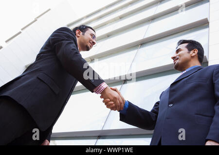 Two businesspeople outdoors by building shaking hands (high key/selective focus) Stock Photo