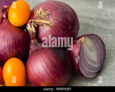 Close-up of group of red onions and two small yellow snack tomatoes. One onion sliced. Selective focus Stock Photo
