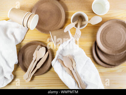 Brown paper cups, plates, wooden cutlery, white linen napkins on wooden background. Recycling concept. Top down view, horizontal image Stock Photo