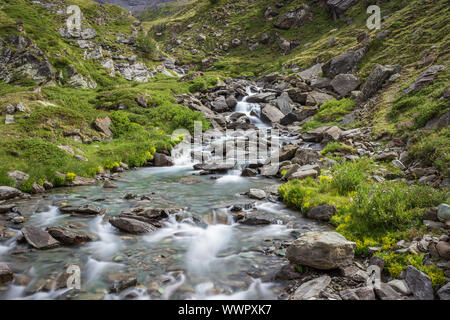 Hiking trail in Aosta valley with wild mountain stream landscape. Long exposure shot.