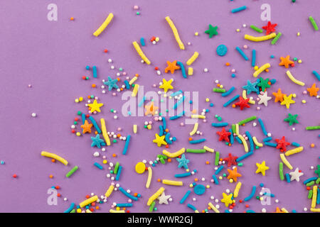 Sprinkle background with rainbow sprinkle shapes, stars, stripes, little balls on lilac background, close up top view photo Stock Photo