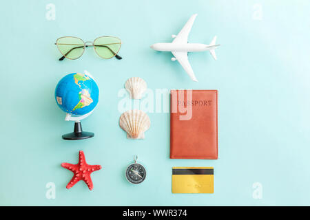 Vacation travel adventure trip concept. Minimal simple flat lay with plane passport sunglasses globe gold credit card and shell on blue pastel colourful trendy background. Tourist essentials Stock Photo