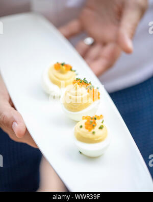 woman serving small platter with three deviled eggs Stock Photo