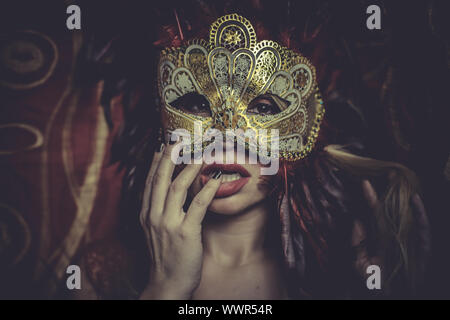 Blonde with gold mask on red cloth embroidered golden thread, mystery and sensuality Stock Photo