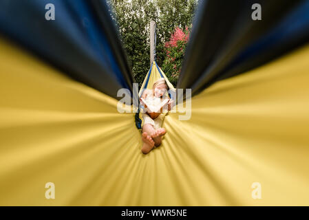 Happy tween girl reading in a yellow hammock Stock Photo