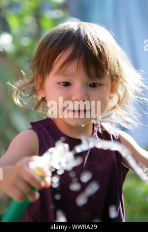 Toddler playing with garden hose Stock Photo