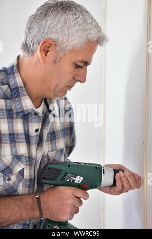 Grey- haired man drilling hole in wall Stock Photo