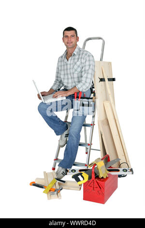 Handyman sitting on a ladder with laptop Stock Photo