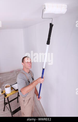 Decorator using a roller extension to paint a ceiling white Stock Photo