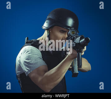 Security, paintball sport player wearing protective helmet aiming pistol ,black armor and machine gun over blue chroma backgroun Stock Photo