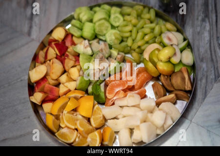 A plate or thali full of fruits such as orange, apple, cucumber, grapes, jicama etc for pooja or puja prasad. Background picture for tropical fruit bo Stock Photo