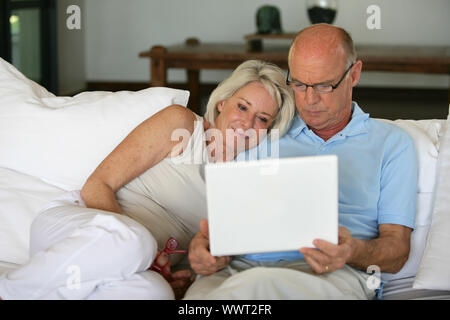 Middle-aged couple sat on sofa with laptop Stock Photo