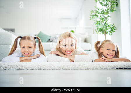 Portrait of three nice cute lovely adorable attractive charming cheerful cheery people pre-teen girls mom mum mommy lying on carpet in light white Stock Photo