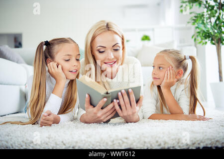 Portrait of three nice cute clever smart lovely sweet attractive charming cheerful people pre-teen girls mom mum mommy lying on carpet reading in Stock Photo