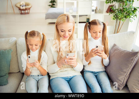 Portrait of nice stylish trendy cute attractive lovely lovable winsome people mum girls sitting on divan using cell in light white interior room Stock Photo