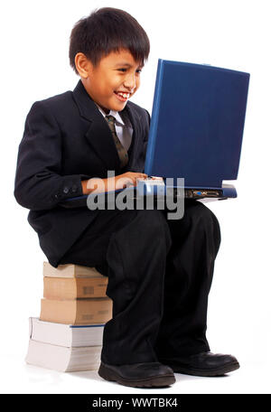 Boy On His Computer Studying For School And Sitting On A Pile Of Books Stock Photo