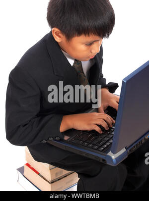Boy Sitting On A Pile Of Books Doing His Homework On A Computer Stock Photo