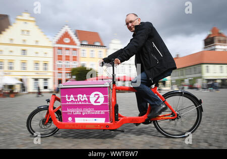 Greifswald, Germany. 16th Sep, 2019. A man rides a freight bike through the old town of Greifswald. Dragged recording with wipe effect. From 16 September 2019, three different load bikes can be borrowed free of charge in Greifswald as part of the EU project 'Cobium' (Cargo bikes in urban mobility). The project aims to analyse the areas in which the use of load bikes makes economic, social and ecological sense and can ultimately replace motor vehicle journeys. Three other cities in the southern Baltic region are involved, Växjö in Sweden, Gdynia and S·upsk in Poland. Credit: dpa picture allianc Stock Photo