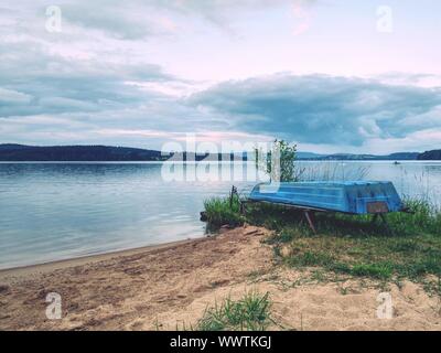 Lonely fishing vessel boat docked on beach at calm lake. Laminate or wooden fishing boat in a still lake water Stock Photo