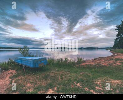 Lonely fishing vessel boat docked on beach at calm lake. Laminate or wooden fishing boat in a still lake water Stock Photo