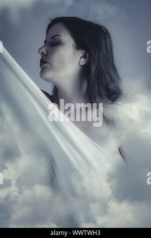 Beautiful woman in clouds, mithology concept. Brunette with long hair and white dress. Stock Photo