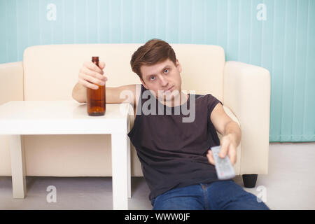A drunk guy with a bottle of beer, the TV changes channels, sitting on the floor Stock Photo