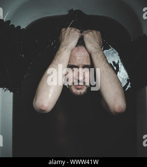 Halloween, Fallen angel, man in a bathtub with black water and wings, submerged, depression, loss Stock Photo