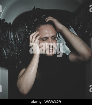 Fallen angel, man in a bathtub with black water and wings, submerged, depression, loss Stock Photo