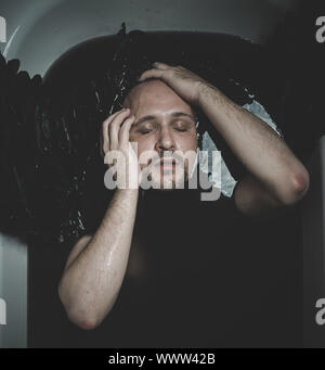 Fallen angel, man in a bathtub with black water and wings, submerged, depression, loss Stock Photo