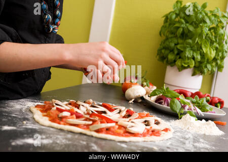 A young female making an italian style pizza at home in her apartment kitchen. - Shallow depth of field is used, with focus on the pizza and hands. Stock Photo