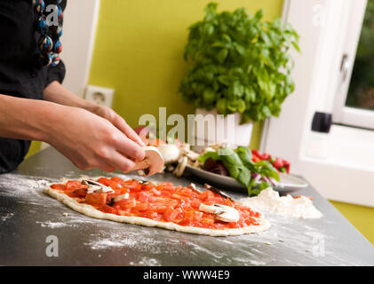 A young female making an italian style pizza at home in her apartment kitchen. - Shallow depth of field is used, with focus on the pizza and hands. Stock Photo