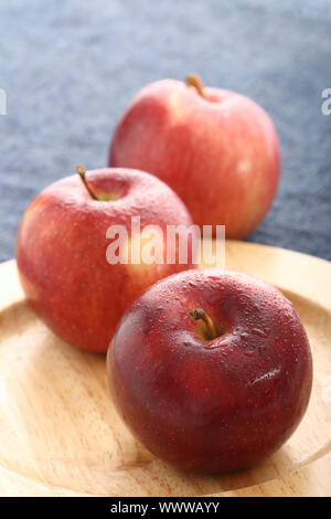 red apples with drops of water on wooden plate with blue denim background Stock Photo