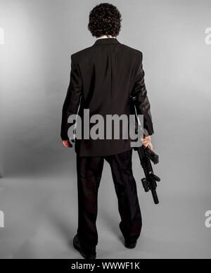 Businessman in black suit and armed with machine gun on gray background Stock Photo