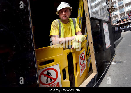 London, England, UK. Worker looking out at the street from a building site in central London Stock Photo