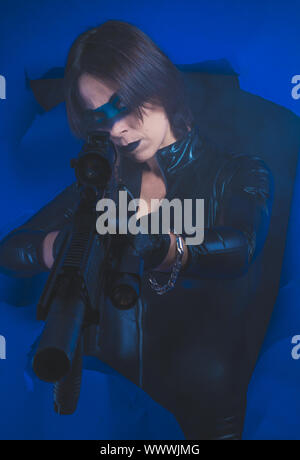 Soldier, Brunette girl dressed in leather and latex fitted with pistol on blue background Stock Photo