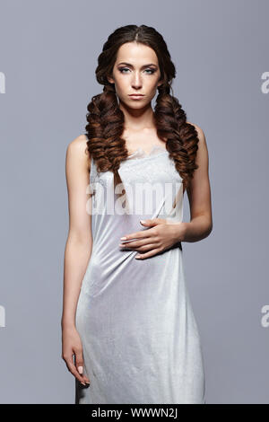 Beauty portrait of young woman in nightie. Brunette girl with long hair plaits and day female makeup on gray background Stock Photo