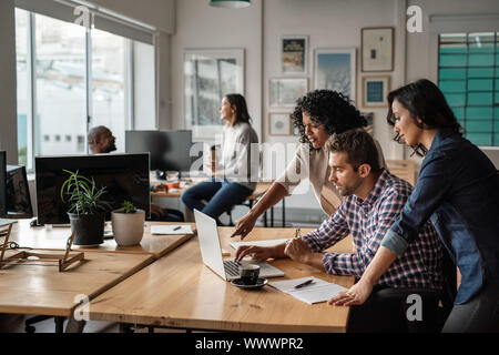 Three young designers using a laptop together at work Stock Photo