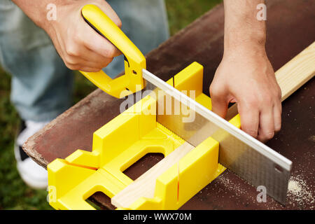 Man cutting a slat of wood using a saw and miter box outdoors. Stock Photo