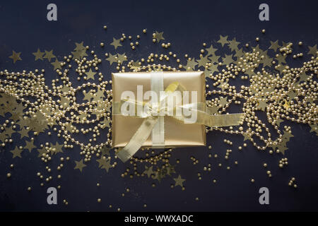 Luxury golden gift box with gold ribbon on shine black background. Christmas, birthday party present. Flat lay. Top view. Festive backdrop. Xmas patte Stock Photo