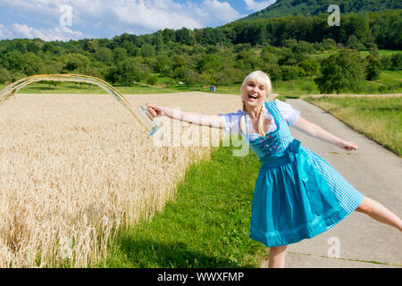 Funny photo of a young woman in a dirndl pour away beer in a field Stock Photo
