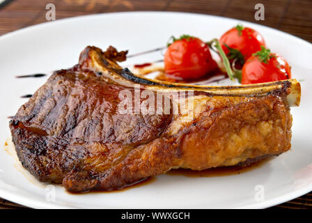 Club Steak. Veal on the bone. Grilled meat ribs on white plate with cherry tomatoes and dark hot sauce