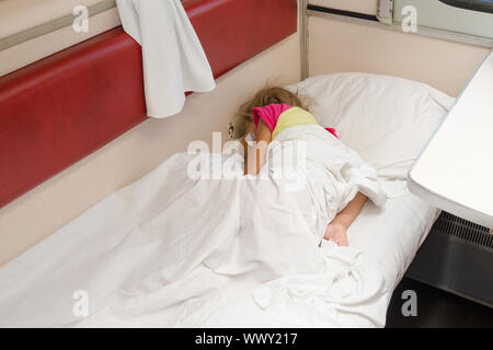 A child in a train sleeping wrapped in a sheet in the lower place in the second-class compartment wagon Stock Photo